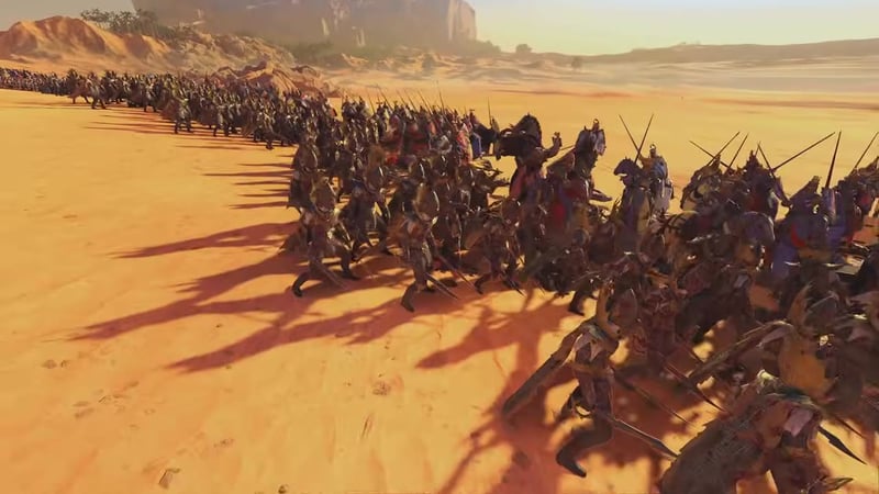 Armored cavalry units, identified by blue and gold banners and livery, charge across a desert battlefield in formation, representing the Bretonnian Knights of the Realm in Total War: Warhammer.